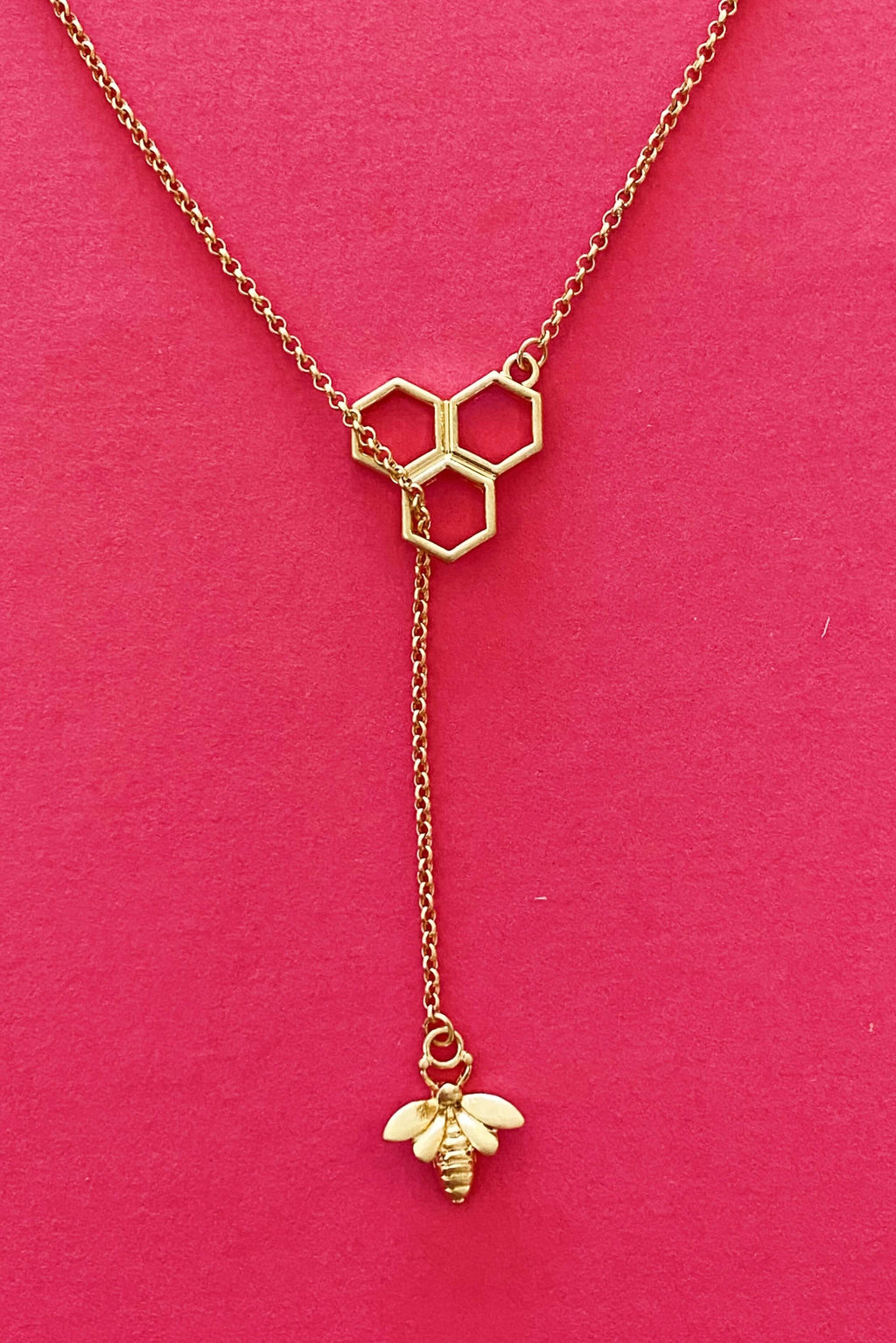 Bee Necklace Gold featuring a stylish hexagon and bee pendant design on a vibrant pink background.