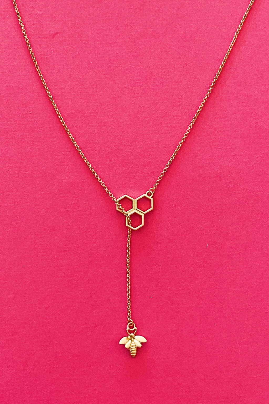 Bee Necklace Gold with hexagon design and bee charm pendant on pink background.